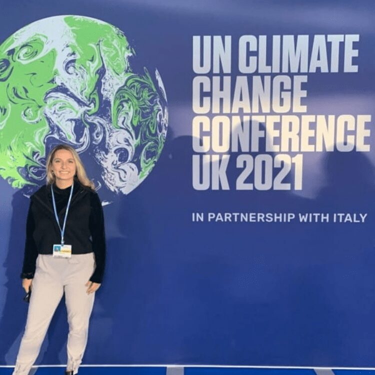 Woman standing in front of a glob and huge sign that says "UN Climate Change conference UK 2021"